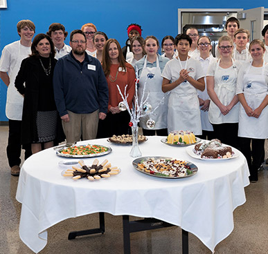 Culinary students standing for a photo with a dining table in front of them with plates of food.